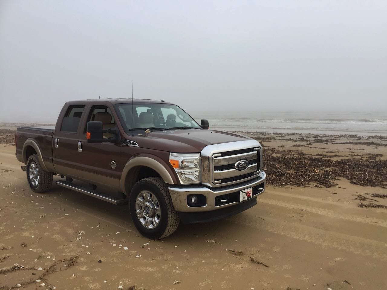 Color photo of a truck on a foggy beach.